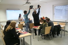Die Teilnehmer an der Aktion "Filmdreh für das E-learning Projekt" simulieren einen typischen Unterrichtsverlauf mit Tablets, das ganze wird gefilmt. Die Teilnehmer sitzen an Tischen und nutzen Lehrbuch, sowie die Tabletts und schreiben auf diesen u.a. Schriftzeichen.
