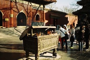 Eine bronzene Truhe mit Räucherstäbchen darin vor einem chinesischen Tempel.